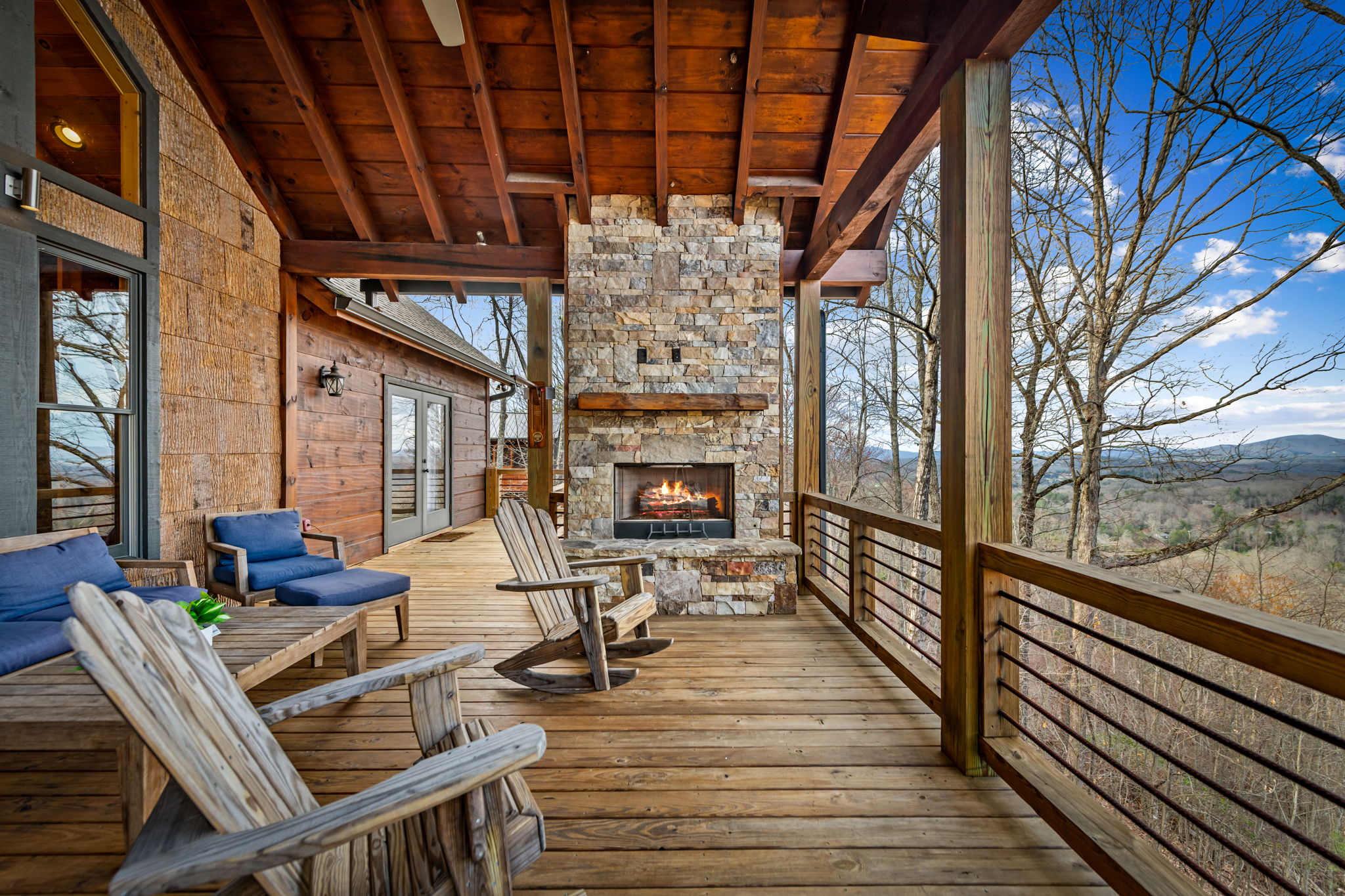 Covered porch with stone outdoor fireplace burning and Adirondack rockers at Eversky on Sunrock Blue Ridge GA